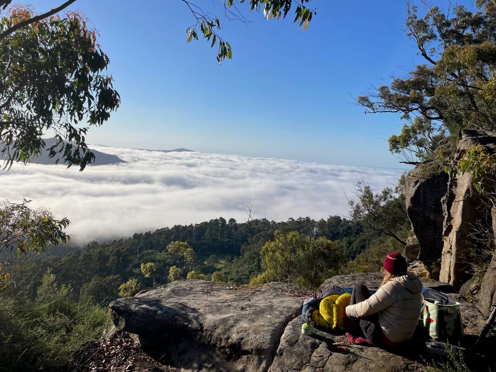 Participant resting at a cliff edge above a cloud-filled valley